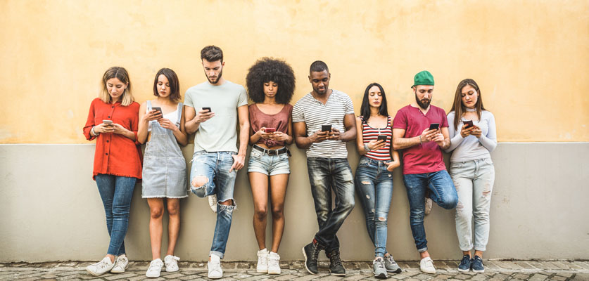 gen z young people standing against wall using mobile devices
