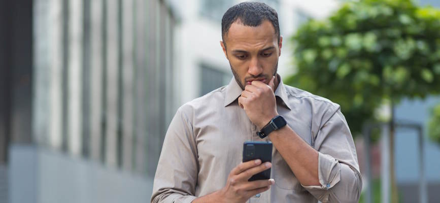 -man looking at his phone with a serious and thoughtful face to show that people are engaged but skeptical of AI adoption the media-