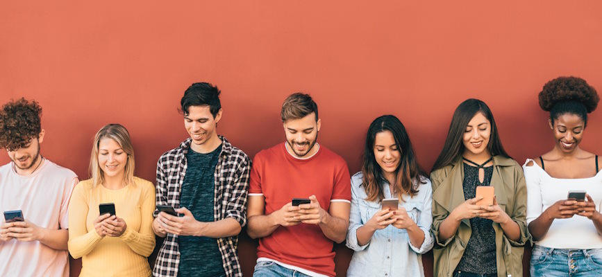 A group of young people smiling looking at phones to demonstrate their trust in news